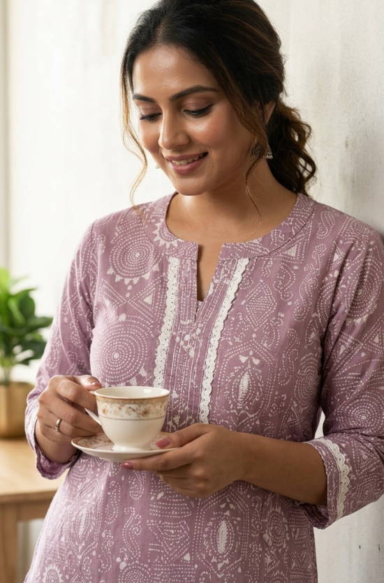 A lifestyle shot of a smiling woman holding a tea cup, wearing a purple ethnic kurta with lace trim.