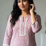 A beautiful portrait of a woman wearing a purple printed kurta with white lace detailing, looking towards the camera.