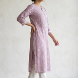 A woman standing sideways wearing a purple printed straight kurta and white pants, showcasing the garment fit.