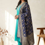 A smiling woman sitting on a sofa wearing a stylish rama green embroidered cotton kurta set with a matching dupatta