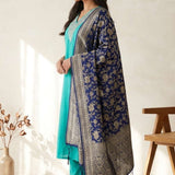A smiling woman sitting on a sofa wearing a stylish rama green embroidered cotton kurta set with a matching dupatta