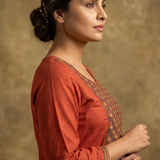 A side-profile view of a woman in a rust-orange embroidered ethnic kurta, showcasing her hairstyle.