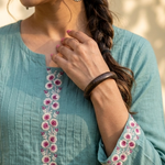 Detailed view of the neckline and sleeve embroidery featuring floral patterns on sea-green cotton fabric.