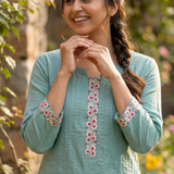 portrait.jpg	A woman posing with her hands near her face, wearing a sea-green embroidered kurta in a garden 