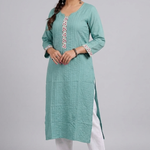 A full-length studio shot of a woman modeling a sea-green straight kurta with white pants. A woman posing with her hands near her face, wearing a sea-green embroidered kurta in a garden sea-green-kurta-walking-shot. A woman walking in a garden wearing a sea-green kurta, show casing the flow and drape of the fabric. sea-green-kurta-tea-lifestyle. A woman holding a clay cup while leaning against a wooden gate, dressed in a sea-green ethnic kurta.