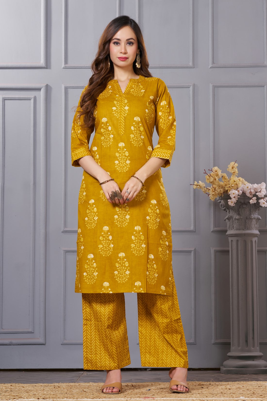 Front full length view of a model wearing an ochre yellow straight fit floral print cotton kurta set with coordinating chevron pants and a printed dupatta