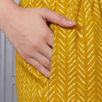 Close up view of the functional side utility pocket stitched seamlessly into a teal floral cotton straight kurta, showing a hand resting inside the pocket over contrasting purple chevron print trousers.