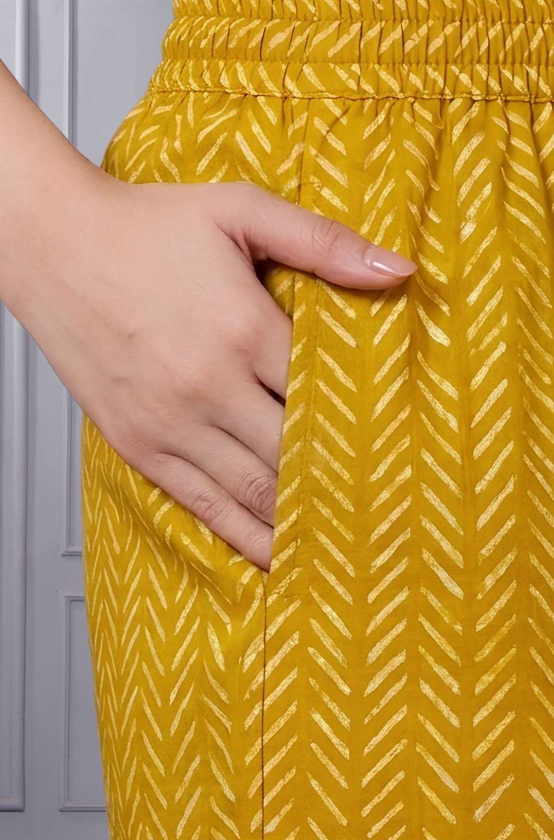 Close up view of the functional side utility pocket stitched seamlessly into a teal floral cotton straight kurta, showing a hand resting inside the pocket over contrasting purple chevron print trousers.