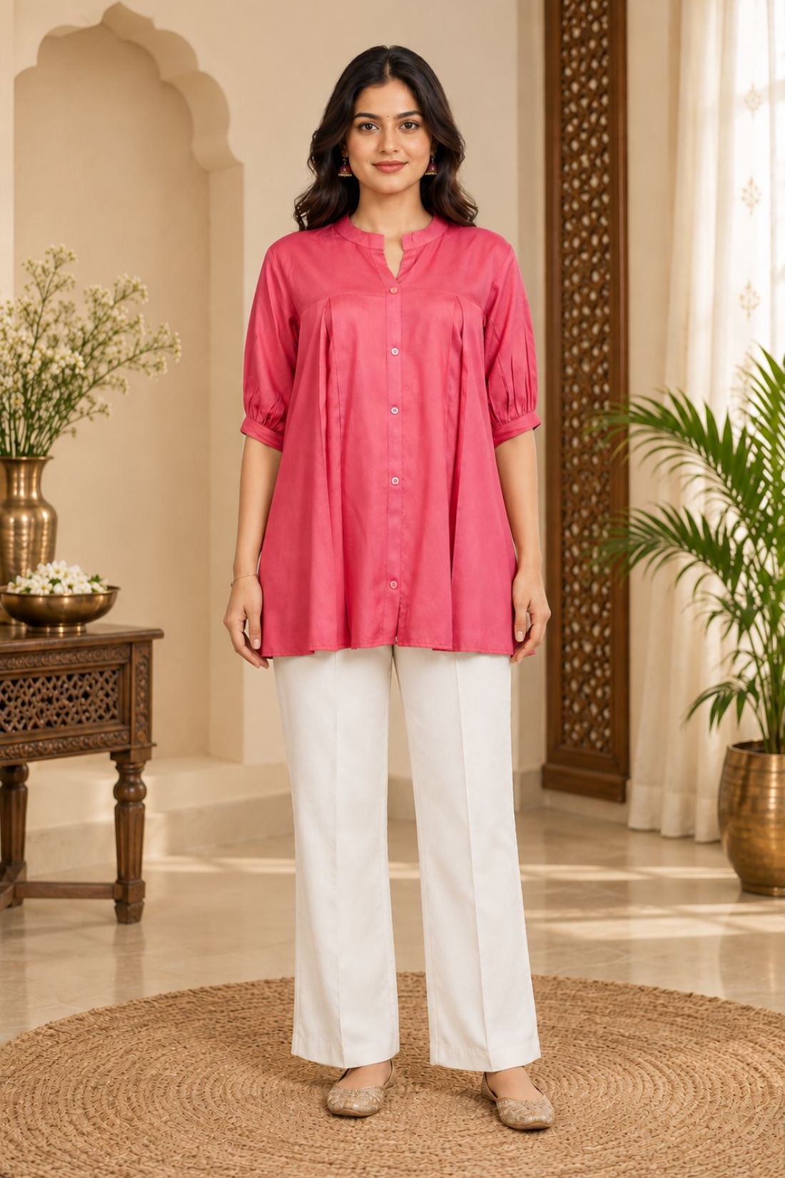 Full-length front view of a woman wearing a dark peach rayon pleated tunic top paired with white straight-leg trousers.