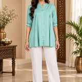 Full-length front view of a model wearing a light sea green rayon pleated top with white trousers.