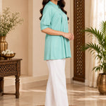 Side profile view of a model posing in a light sea green pleated rayon tunic top with cuffed sleeves.