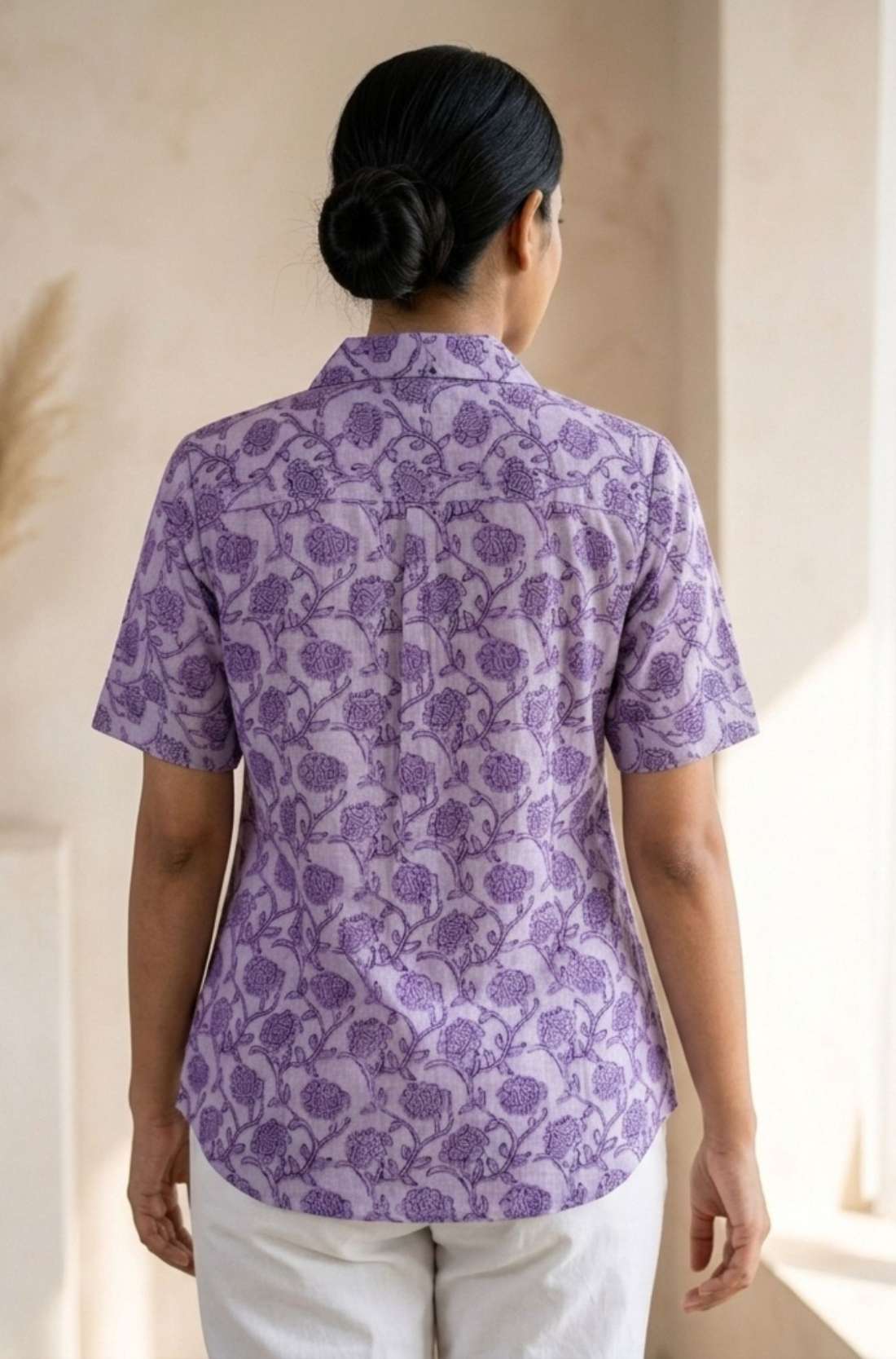Back view of a women's lavender floral block print cotton shirt with short sleeves and curved hem.