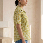 Side profile of a women's yellow floral block print cotton shirt with relaxed fit and collared neckline.