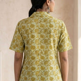 Back view of a women's yellow floral hand block print cotton shirt with curved hem and short sleeves.