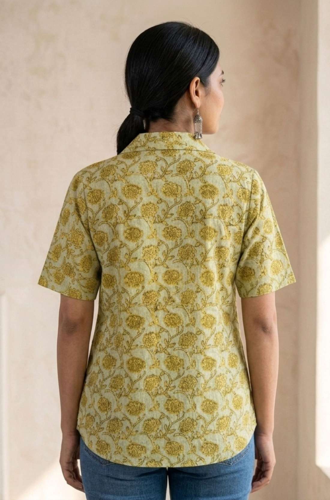 Back view of a women's yellow floral hand block print cotton shirt with curved hem and short sleeves.