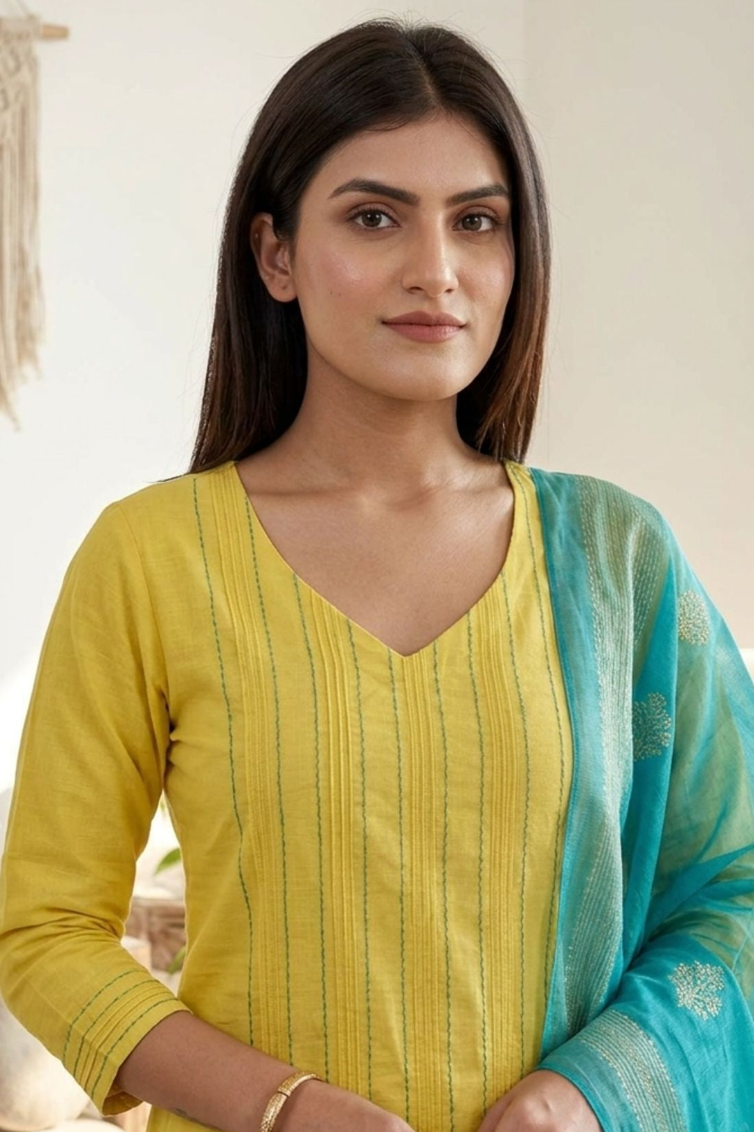 Detailed close-up shot of a bright yellow pure cotton kurta showcasing elegant vertical pintuck detailing with contrast green stitching along the V-neckline, styled with a contrasting turquoise blue dupatta.