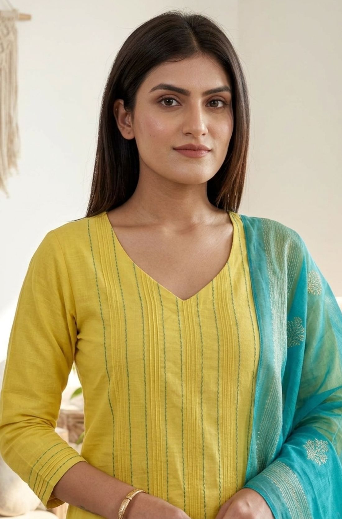 Detailed close-up shot of a bright yellow pure cotton kurta showcasing elegant vertical pintuck detailing with contrast green stitching along the V-neckline, styled with a contrasting turquoise blue dupatta.