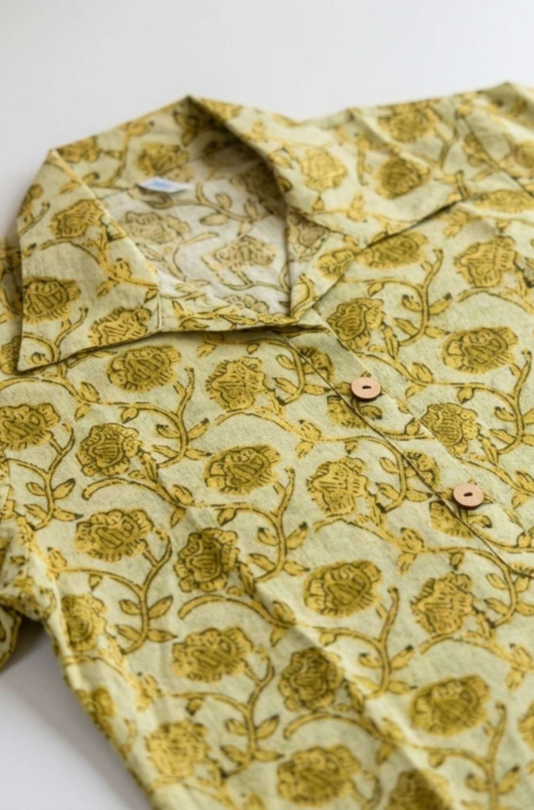 Flat lay of a yellow hand block print cotton shirt featuring floral print, collar, and wooden button placket.